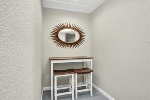 A corner with a white wall, a white table with two wooden stools, and a sunburst mirror above the table. - Holds 8 · Pool · 3BR/2BA Lower-Unit Duplex Peacock Horse Beach NearbyOut of City (Galveston)