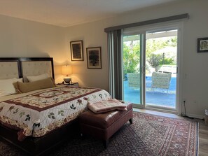 Una camera da letto con un letto grande, un comodino con una lampada e una porta scorrevole in vetro che dà su un patio esterno con sedie.