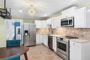 A kitchen with white cabinets, a stainless steel refrigerator, a microwave, a stove, and a sink.