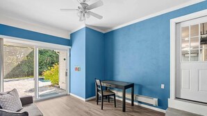 A room with a blue wall, a ceiling fan, a dining table with chairs, and a sliding glass door leading to an outdoor area. - Charming Hampton Bays Home Near Beaches (Hampton Bays)