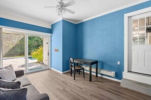 A room with a blue wall, a ceiling fan, a dining table with chairs, and a sliding glass door leading to an outdoor area. - Charming Hampton Bays Home Near Beaches (Hampton Bays)