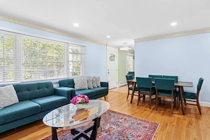A living room with a sofa, a glass coffee table, and a dining area with chairs and a table.