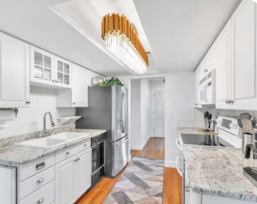 A modern kitchen with white cabinetry, granite countertops, stainless steel appliances, and a unique ceiling light fixture.
