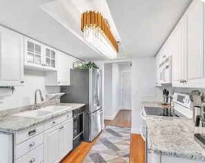 A modern kitchen with white cabinetry, granite countertops, stainless steel appliances, and a unique ceiling light fixture. - Main house and guest house, Events, Heated Pool 15min to Clw Beach (Clearwater)