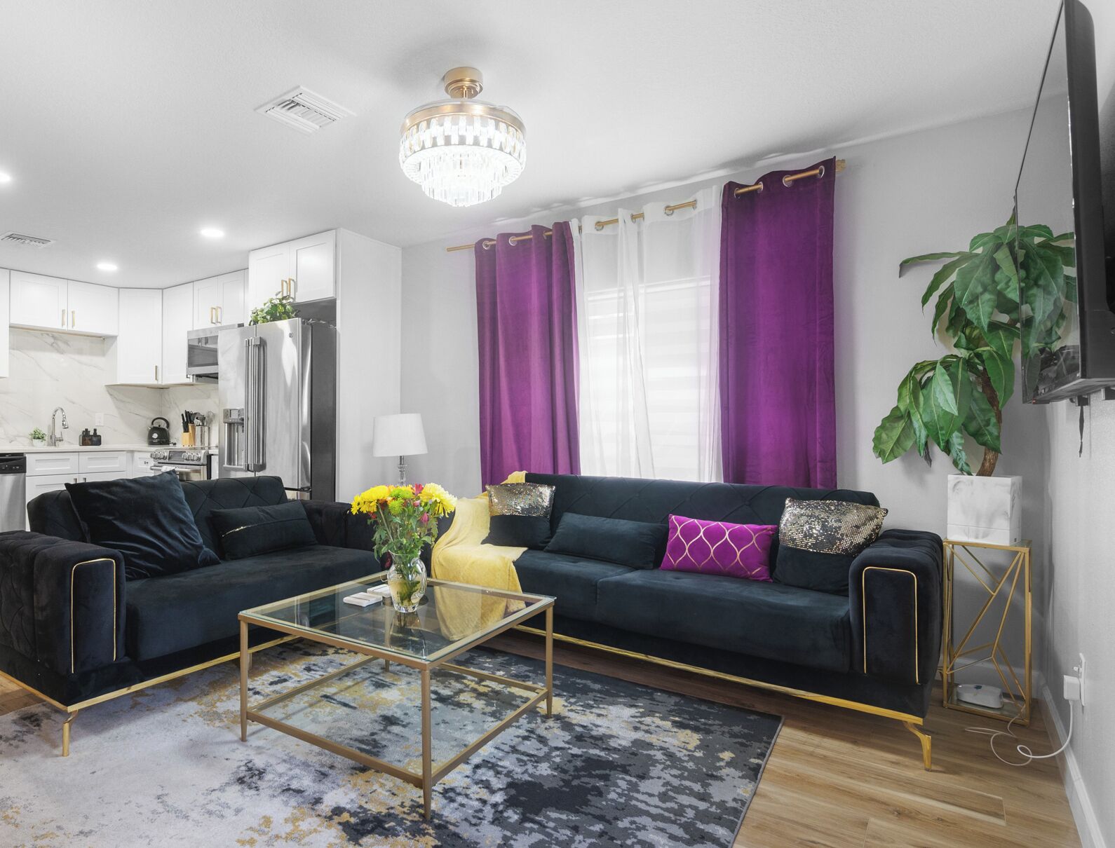 A modern living room with a dark green sofa, a glass coffee table, and a chandelier.