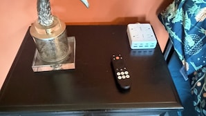 Una mesita pequeña con un control remoto, un objeto decorativo y una regleta.