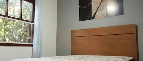 A room with a bed, a window, and a wall-mounted artwork.
