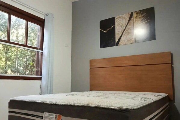 A room with a bed, a window, and a wall-mounted artwork.