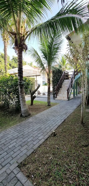 A paved pathway with palm trees, a staircase, and a building in the background. - Feet in the Sand / Beach House / Bertioga (Bertioga)