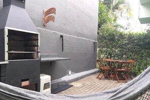 A barbecue grill with a chimney, a small white stool, and a table with chairs in a garden setting.