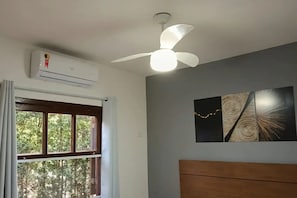 A room with a ceiling fan, an air conditioning unit, a window with curtains, and a bed with a wooden headboard.