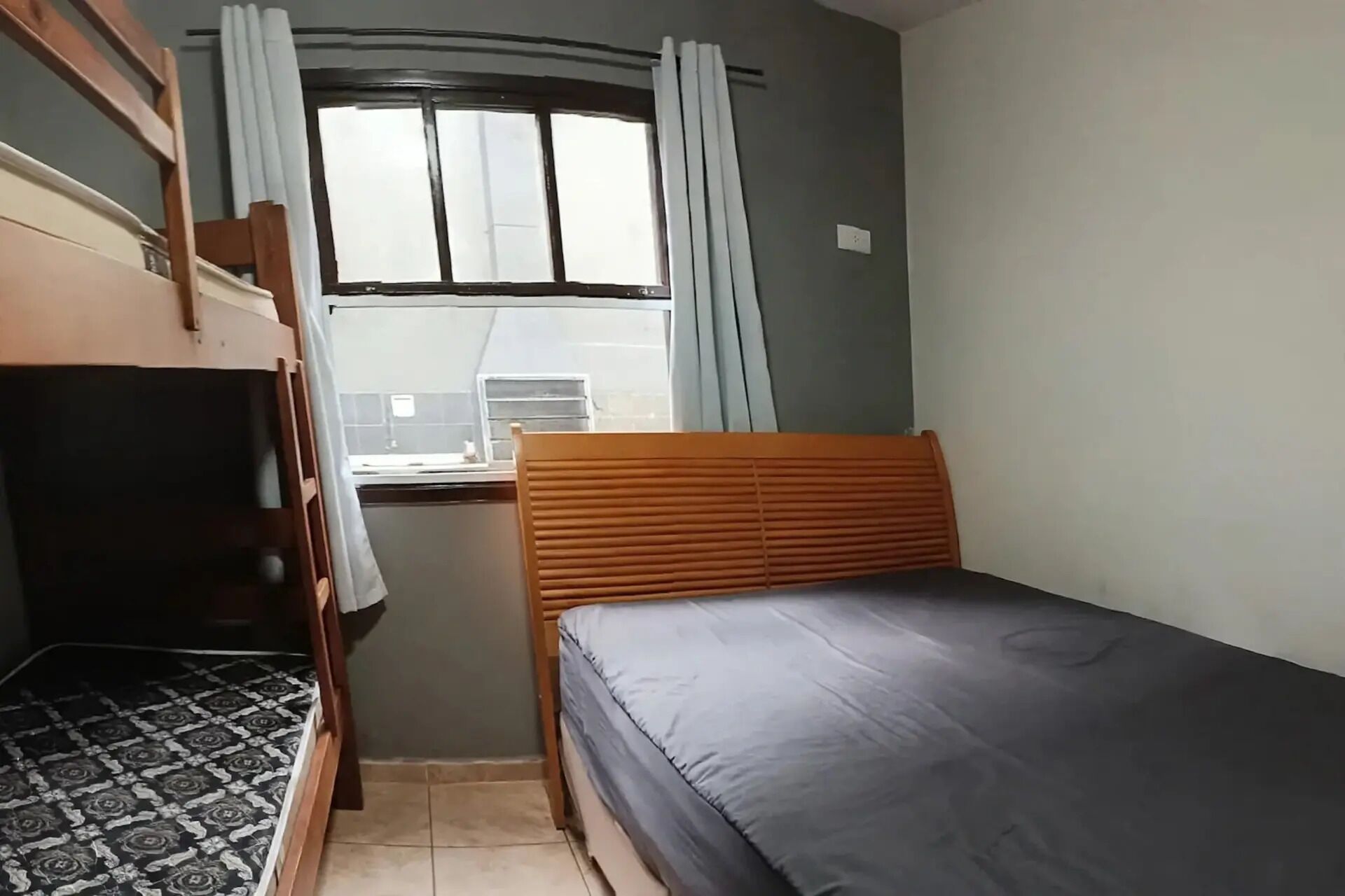 Een kamer met een stapelbed, een enkel bed, een raam met gordijnen, en een bureau met een stoel.
