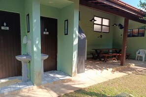 A building with two doors labeled for men and women, a covered outdoor seating area, and a window with a view. - Feet in the Sand / Beach House / Bertioga (Bertioga)