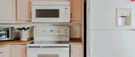 A kitchen with a microwave, oven, and refrigerator, wooden cabinets, and a window with a view of trees.
