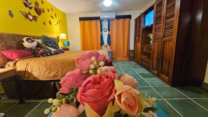 A hotel room with a bed, a wooden wardrobe, a television, and a floral arrangement on the floor. - Frida Kahlo Suite, 1 minute from Playa Oro (Puerto Vallarta)