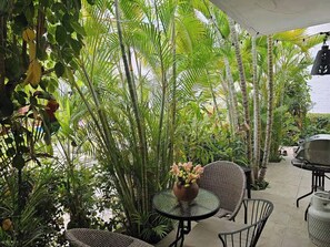 Eine Terrasse im Freien mit Tischen und Stühlen, umgeben von üppiger Vegetation und hohen Palmen.