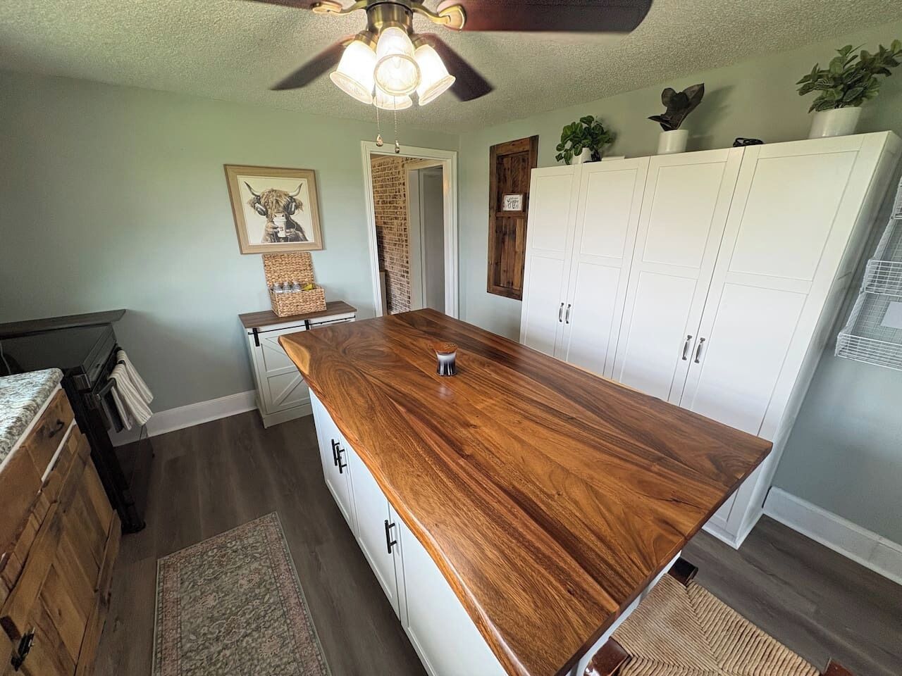 A kitchen with a wooden island, white cabinets, and a ceiling fan.