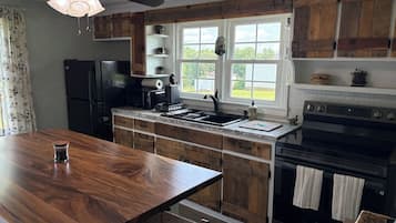 Une cuisine avec des meubles en bois, un réfrigérateur noir, une cuisinière et une fenêtre donnant sur l’extérieur.