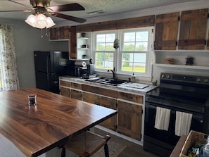 A kitchen with wooden cabinets, a black refrigerator, a stove, and a window with a view of the outdoors.
