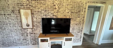 Un soggiorno con parete in mattoni, una TV a schermo piatto su un supporto in legno e un mobile TV bianco con spazio contenitore.