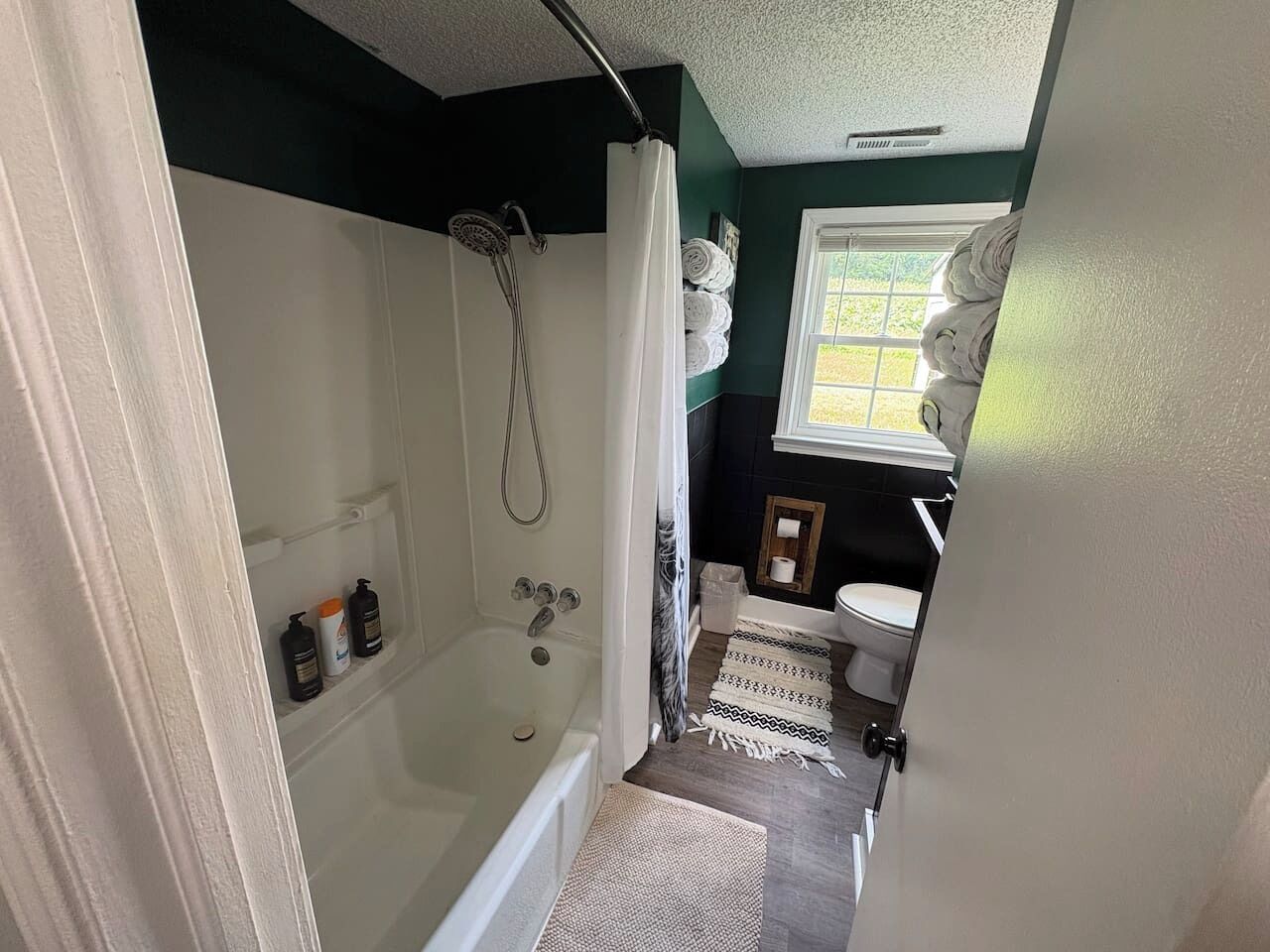 A bathroom with a bathtub, shower, toilet, and a window.