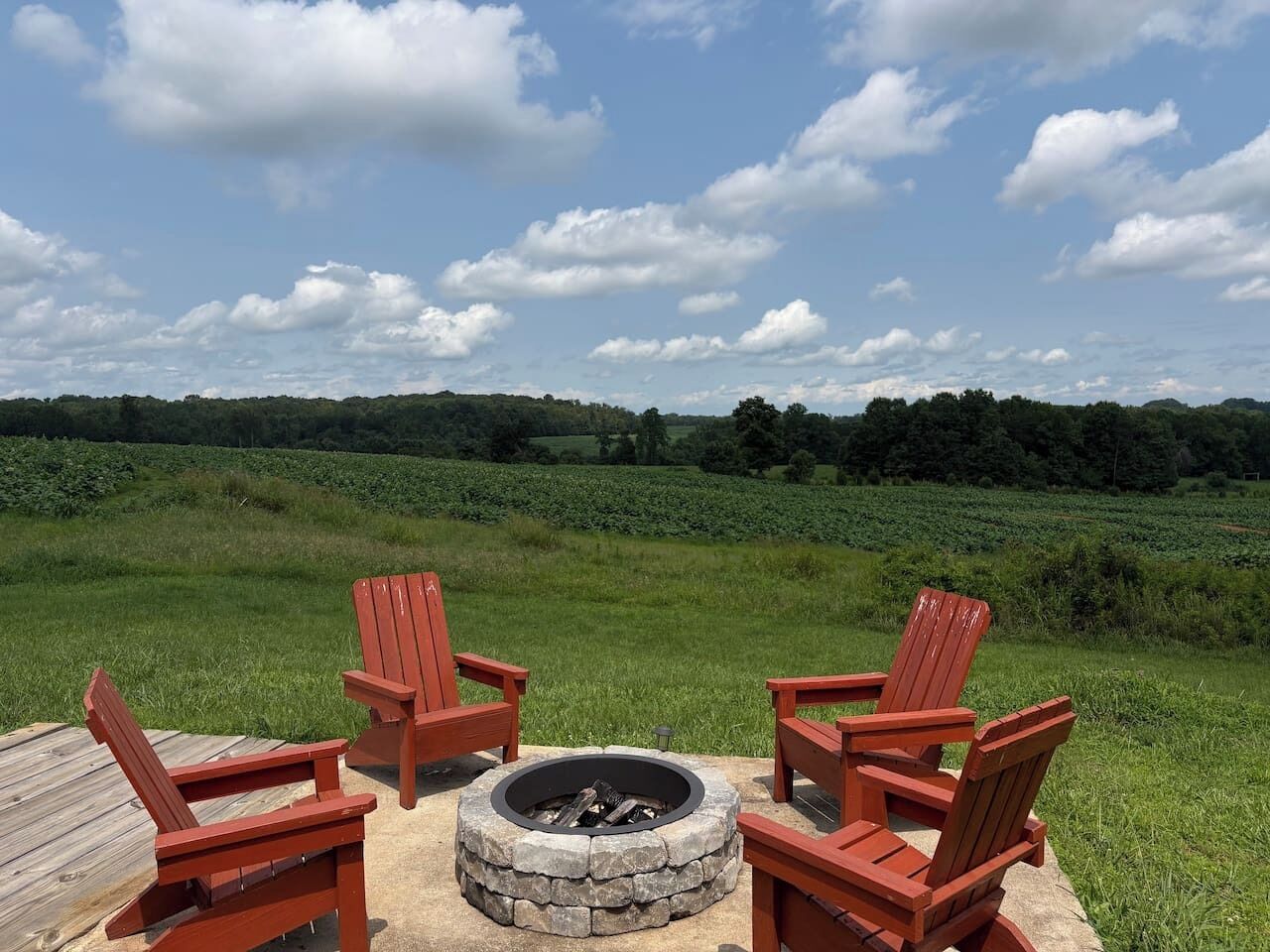 A fire pit with four red Adirondack chairs arranged around it on a wooden deck.