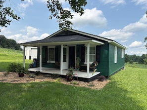 A single-story house with a covered porch, surrounded by a grassy landscape.