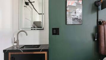 A modern bathroom with a black sink, a mirror, a green wall, and a framed picture.