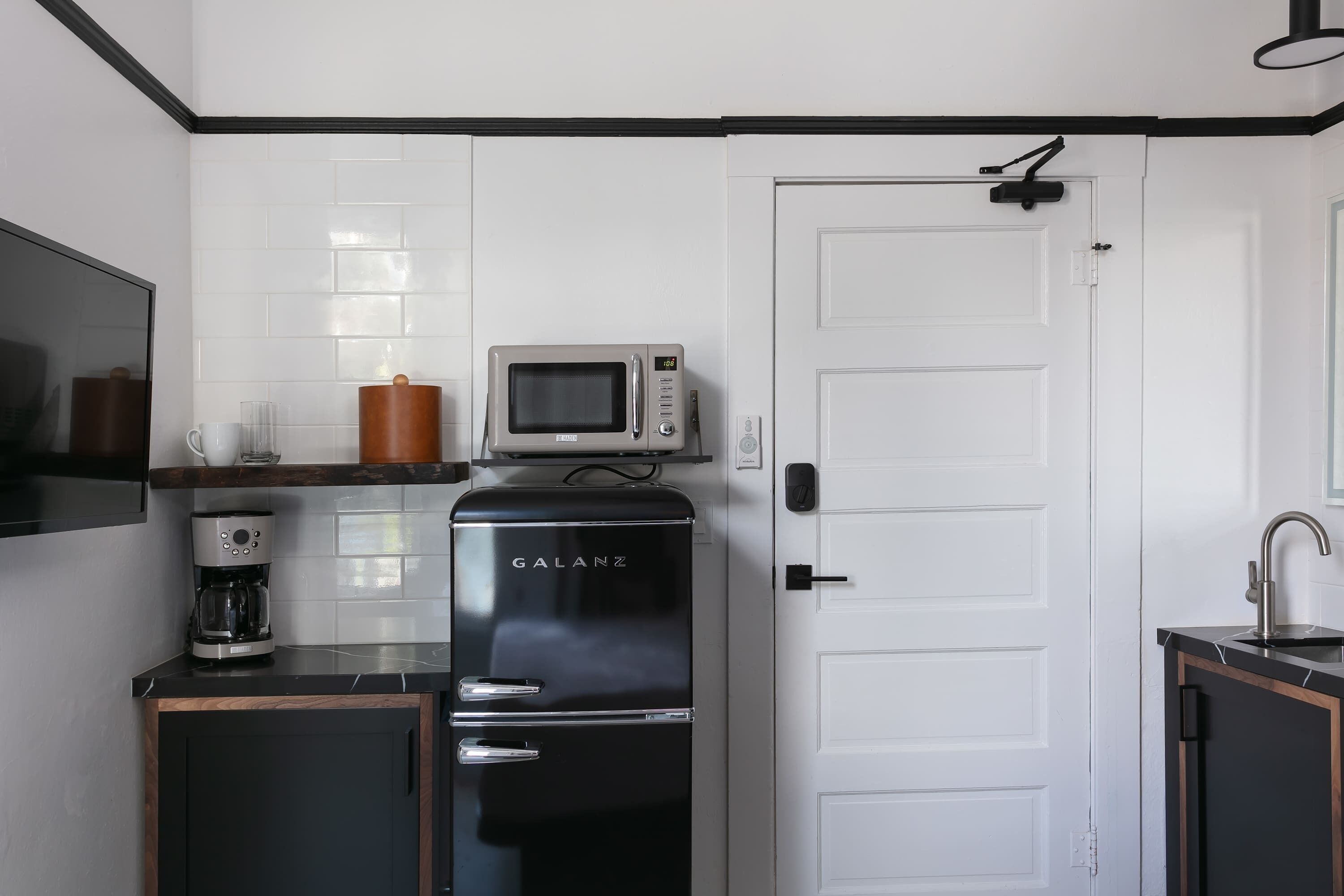 A compact kitchen with a refrigerator, microwave, coffee maker, and a door with a handle.