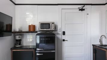 A compact kitchen with a refrigerator, microwave, coffee maker, and a door with a handle.