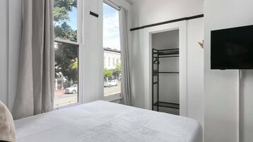 A hotel room with a bed, a television, a wardrobe, and a window with curtains.