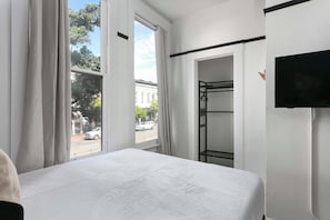 A hotel room with a bed, a television, a wardrobe, and a window with curtains. - La Ventana Hotel - Historic Hotel Stay in the Gaslamp Quarter (San Diego)