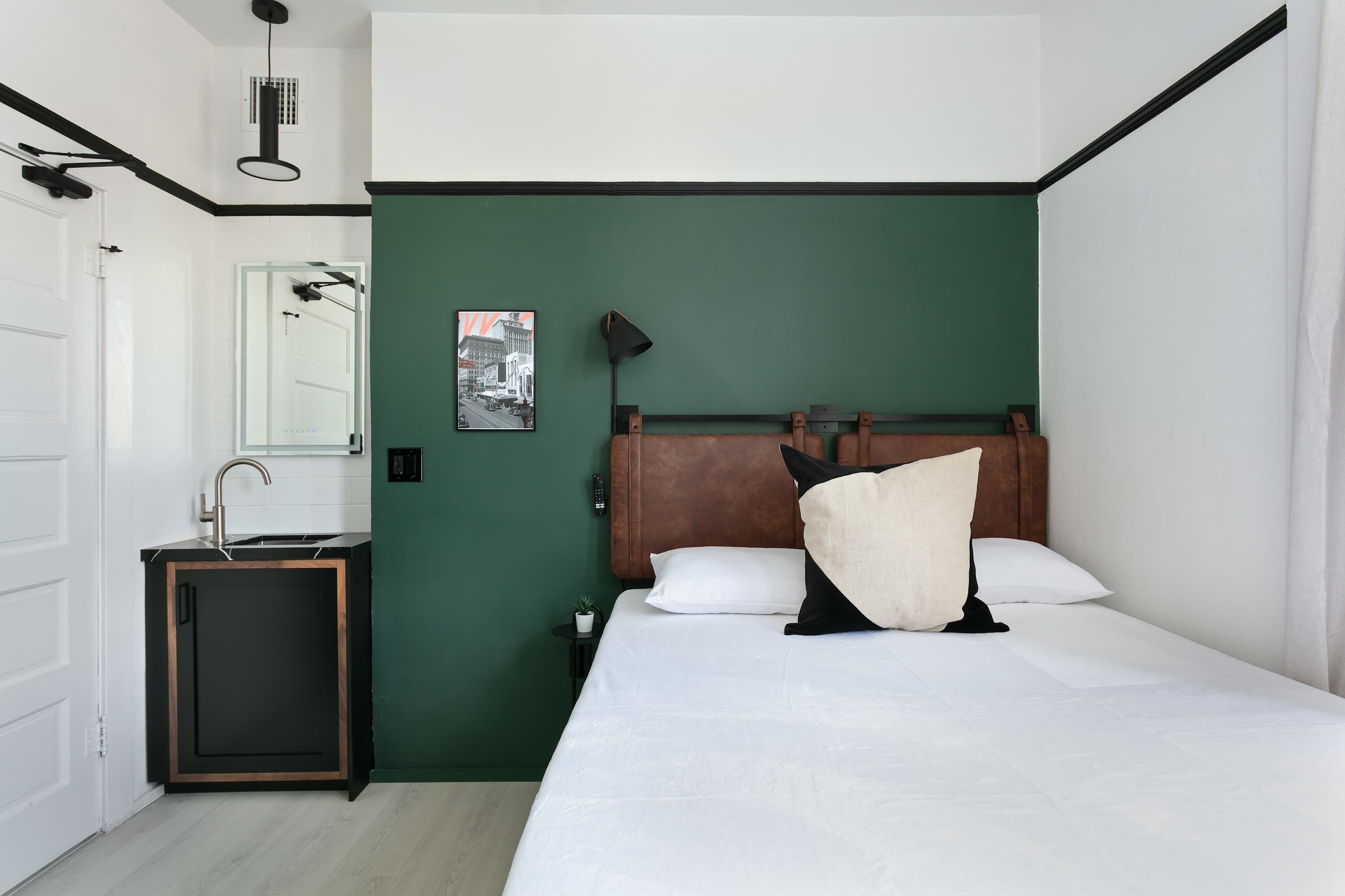Une chambre à coucher comprenant un lit, une table de chevet, une lampe, un tableau accroché au mur et une porte avec un miroir.