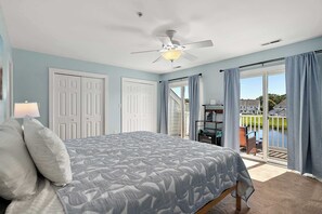 A bedroom with a bed, a ceiling fan, and a view of a pool and house through the window. - Large Waterfront Townhome with Great Amenities (Ocean City)