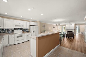 A modern kitchen with white cabinetry, a central island, and a dining area with a fireplace. - Large Waterfront Townhome with Great Amenities (Ocean City)