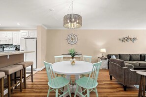 A modern kitchen with white cabinets, a dining area with a round table and chairs, and a living room with a sofa and a lamp. - Large Waterfront Townhome with Great Amenities (Ocean City)