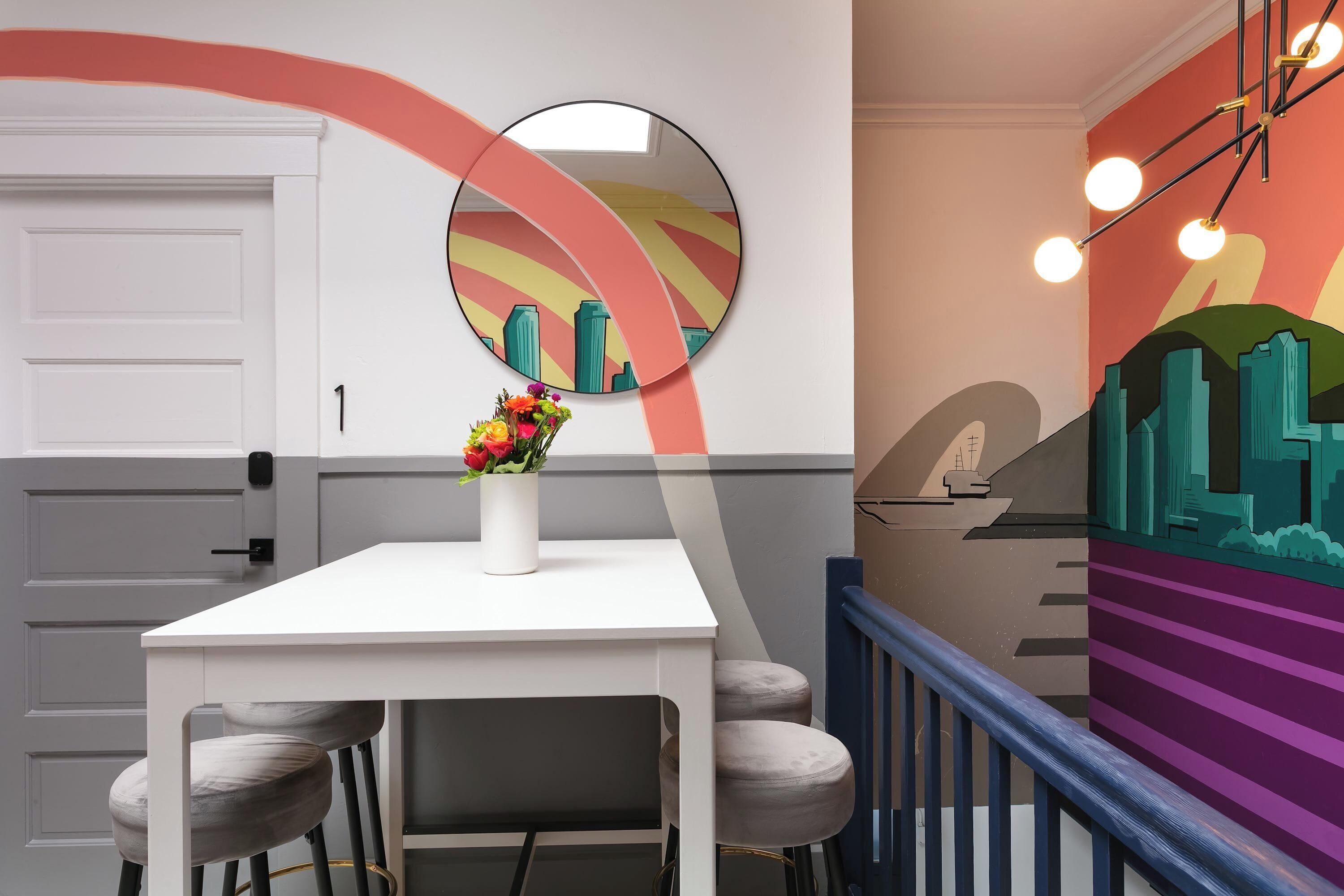 Een modern interieur met een witte tafel, een bloevas, een ronde spiegel en een kleurrijke muurschildering.