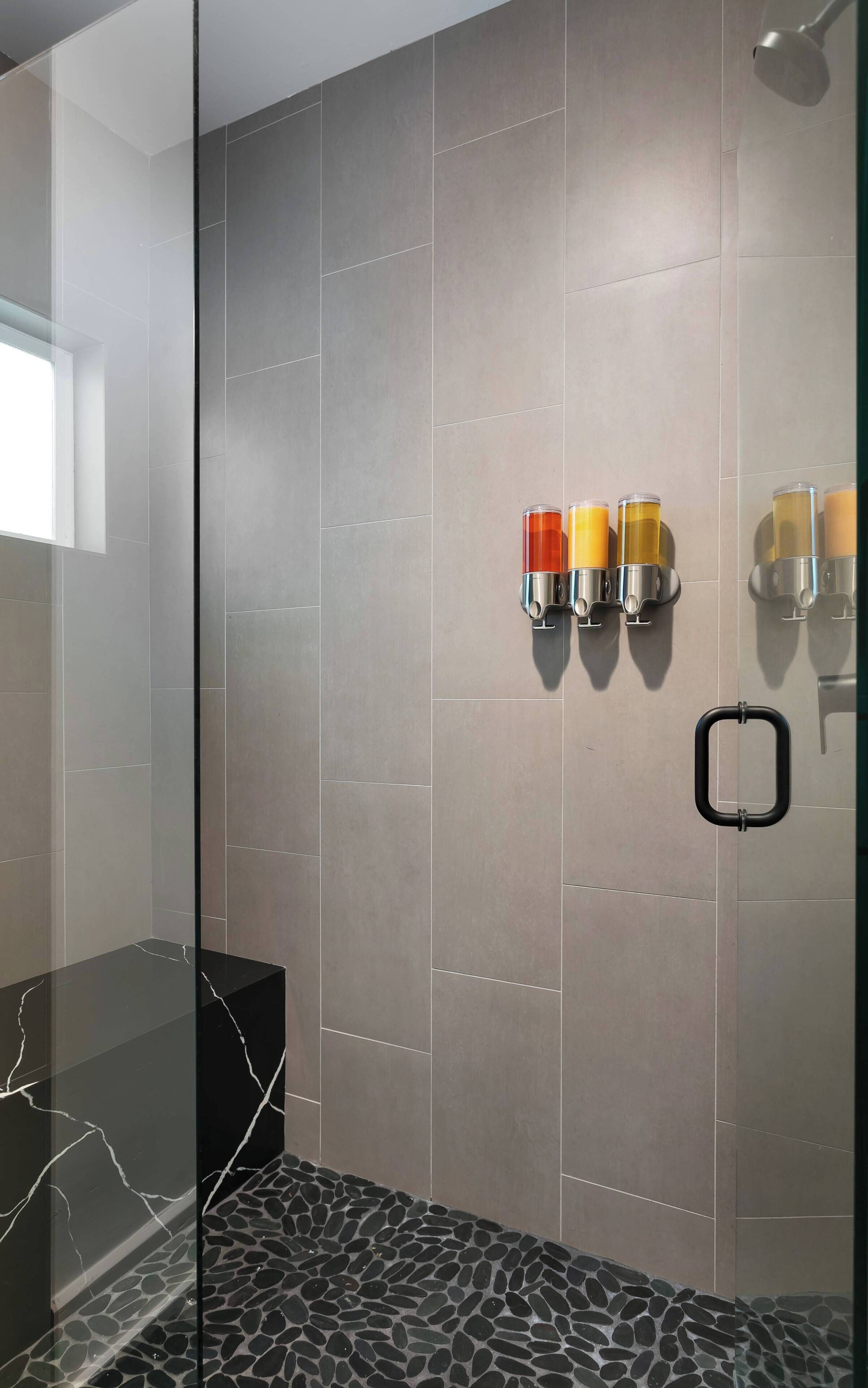 A modern bathroom with grey tiles, a glass shower enclosure, and a marble vanity.