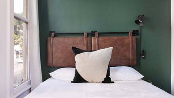 A bed with a headboard against a green wall, a window on the left, and a wall-mounted lamp.
