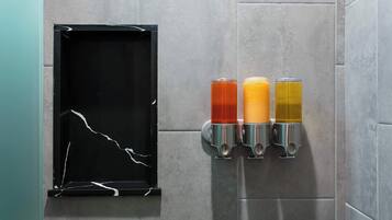 A wall-mounted beverage dispenser with three different colored drinks, a black-framed mirror, and a tiled wall.