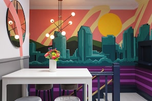 A modern interior with a cityscape mural, a white table, and bar stools. - La Ventana Hotel - 1BR Escape Queen Bed, WiFi & Kitchenette (San Diego)