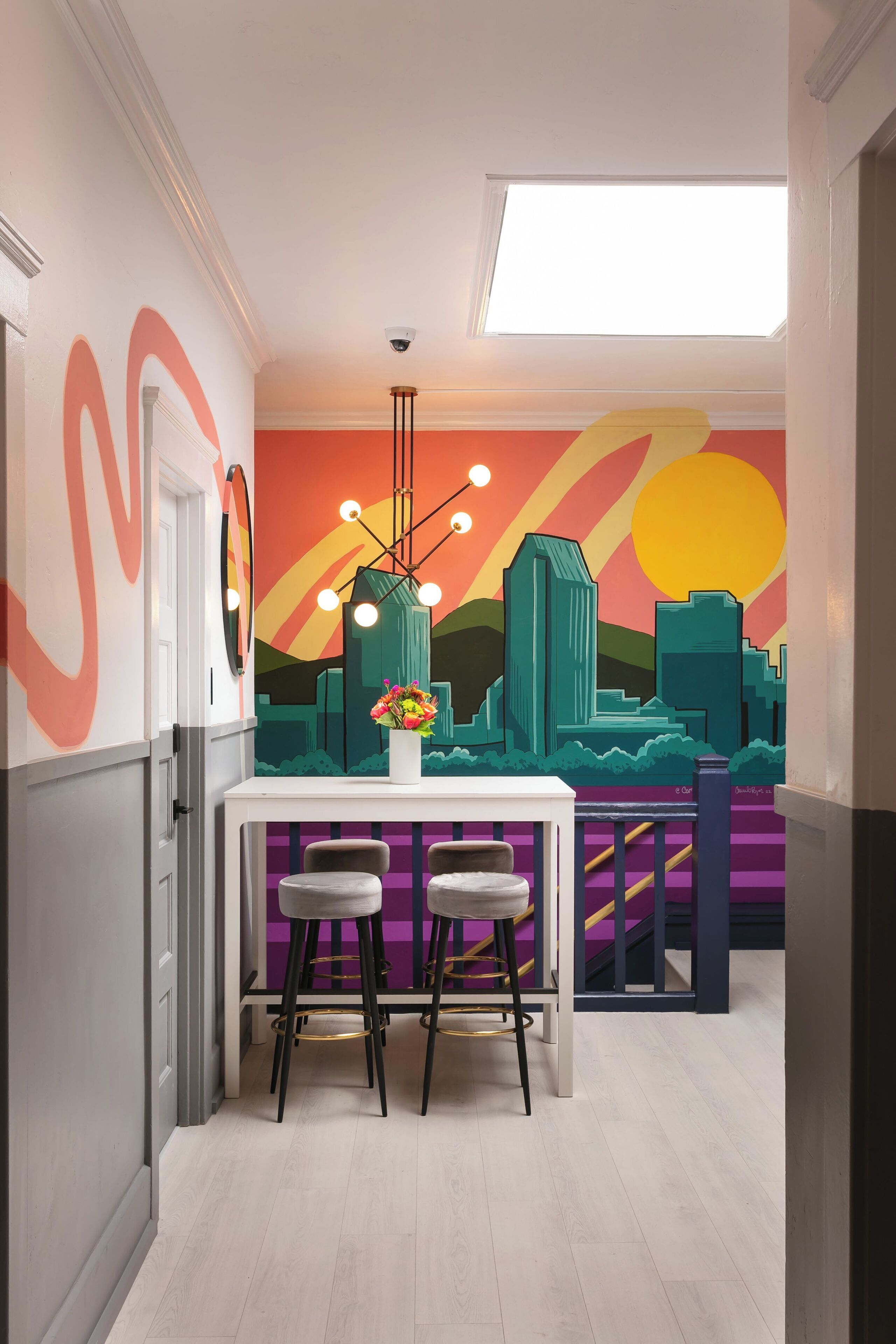 Een moderne keuken met een wit aanrecht, twee barkrukken en een stadsgezicht op de muur.