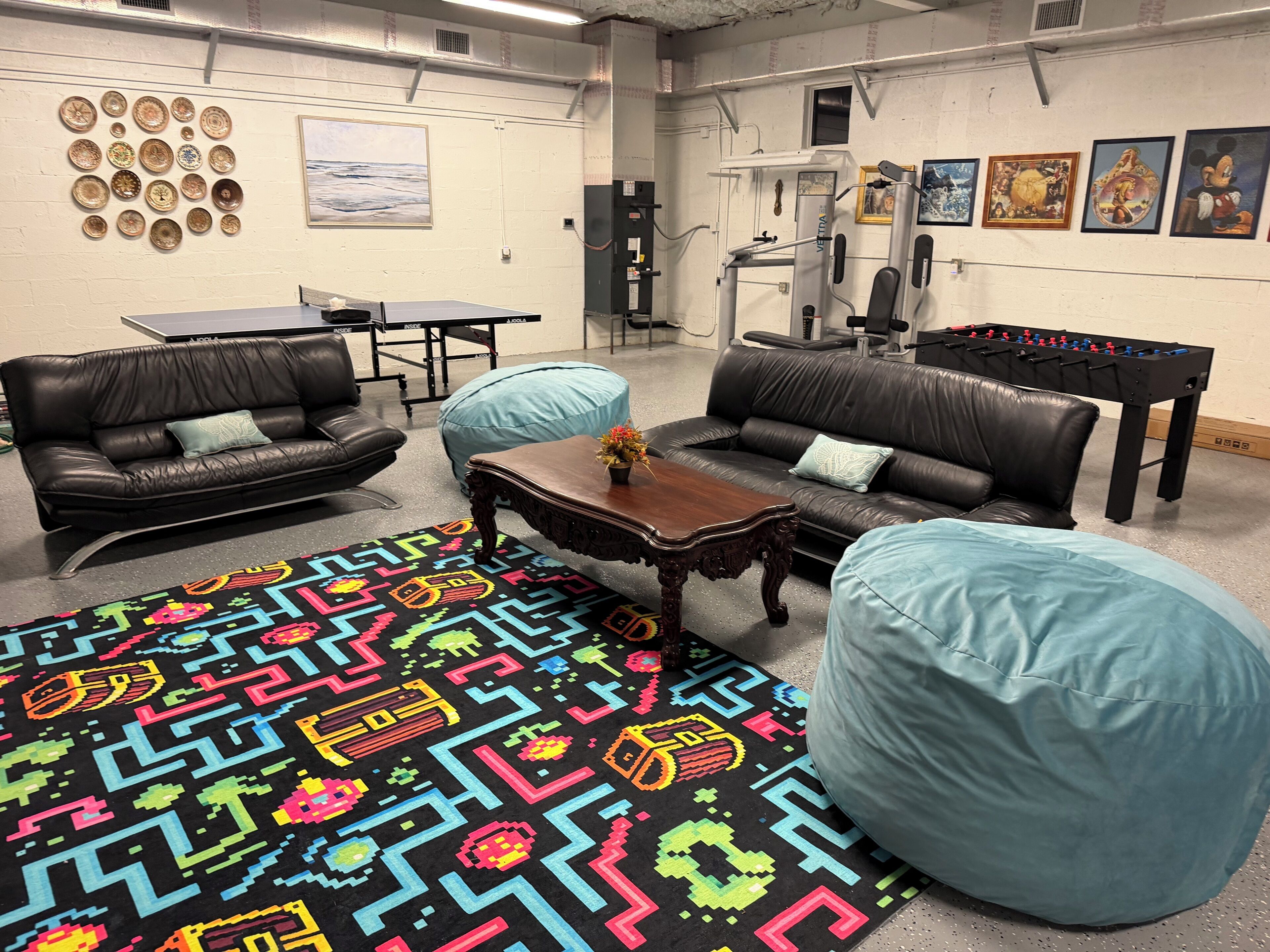Una habitación con dos sofás de cuero, una mesa de fútbol de mesa y una mesa de ping pong, además de una alfombra colorida.