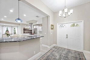 A spacious kitchen with a marble countertop, pendant lighting, and a view into the dining area. - Heated Pool Hot Tub Game Room Jupiter Farms Home (Jupiter)