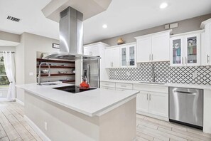 A modern kitchen with a central island, stainless steel appliances, and white cabinetry. - Heated Pool Hot Tub Game Room Jupiter Farms Home (Jupiter)