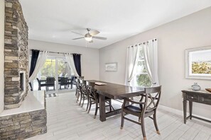 A dining area with a long table, chairs, a ceiling fan, and a stone wall. - Heated Pool Hot Tub Game Room Jupiter Farms Home (Jupiter)