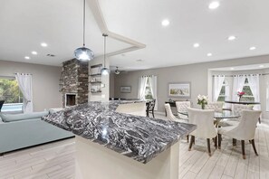 A modern kitchen with a marble island, dining area with white chairs, and a stone accent wall. - Heated Pool Hot Tub Game Room Jupiter Farms Home (Jupiter)