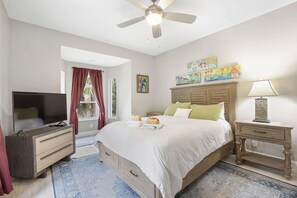 A bedroom with a bed, a television, a nightstand, and artwork on the wall. - Heated Pool Hot Tub Game Room Jupiter Farms Home (Jupiter)
