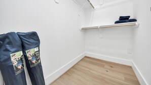 Ein Zimmer mit weißer Wand, Holzboden, einem weißen Regal und einer dunkelblauen Hose, die an einem Haken hängt.