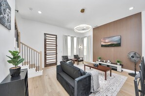 Ett modernt vardagsrum med en soffa, ett soffbord, en tv och en vägg som har en träpanel som accent.